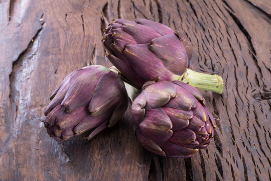 Green and purple artichoke flower edible buds on wooden background.