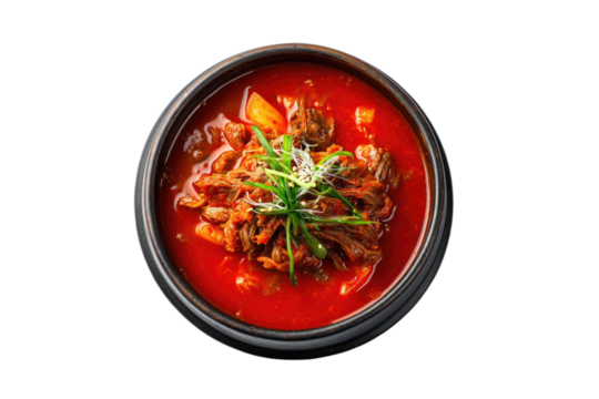 Top-down view of a dark bowl filled with spicy red stew, beef, and chopped scallions