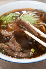 Taiwanese beef noodle soup, famous food in a bowl on wooden table.
