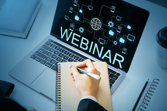 Online webinar training session with person taking notes on notepad in front of laptop screen displaying digital connection graphics on dark background.