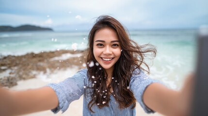 Woman enjoys a sunny day at the beach while taking a selfie near the calm waves of the ocean and rocky shoreline