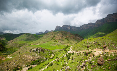 Fototapeta premium a majestic mountain range with distinct stratified rock formations and green slopes. Foreboding clouds loom overhead, a storm brewing, to the dramatic effect of the rugged landscape.