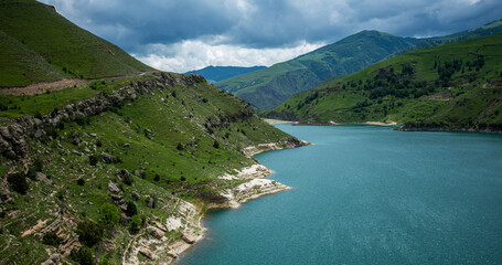 Turquoise lake nestled in green mountainous terrain, under a dramatic cloudy sky, showcasing nature's contrast between water and land