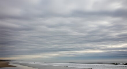 Fototapeta premium Cloudy beachscape waves meet sandy shore beneath an overcast sky