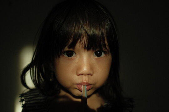 Portrait of a young girl sipping a drink through a straw, captured with dramatic low-key lighting and soft shadows. The light highlights her eyes and facial expression, creating an intimate and moody - Powered by Adobe