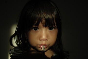 Portrait of a young girl sipping a drink through a straw, captured with dramatic low-key lighting and soft shadows. The light highlights her eyes and facial expression, creating an intimate and moody
