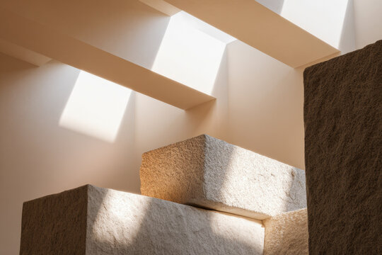 Sunlight streaming through skylights illuminates textured beige stone blocks creating an abstract geometric composition in a minimalist architectural interior space