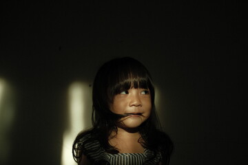  Portrait of a young girl with windblown hair illuminated by a dramatic beam of sunlight. Soft shadows emphasize her thoughtful expression in a cinematic indoor setting.