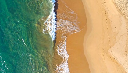 Aerial view of ocean waves lapping a golden sandy beach with footprints visible