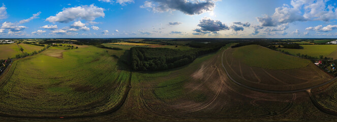 Wide landscape, fields, forests and clouds under a sunny sky in a rural setting.