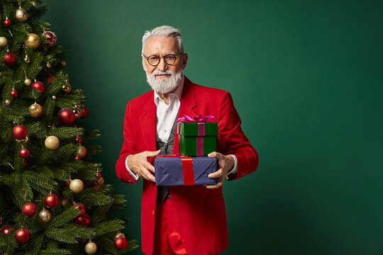 Senior man holds colorful gifts by a beautifully decorated Christmas tree - Powered by Adobe