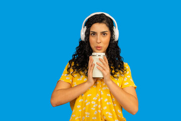 Woman with headphones blowing on hot coffee mug