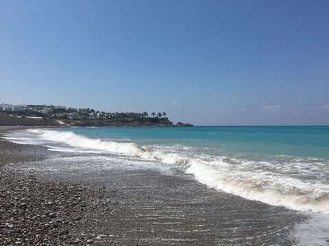 Tranquil Seaside Landscape with Gentle Waves and Clear Blue Sky near Rocky Shoreline