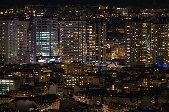 Aerial view of a dark cityscape with buildings lit up at night, creating a warm glow against the inky sky, Paris, Ile-de-France, France.