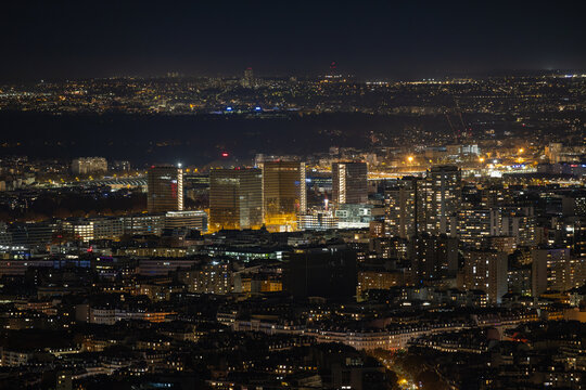 Aerial view of glimmering lights dance across the Parisian skyline, illuminating modern skyscrapers against the velvet night, Paris, Ile-de-France, France.