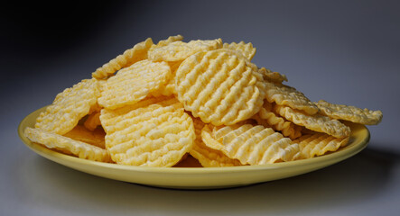 A pile of corn chips on a yellow plate. Round corn chips. Ribbed chips.