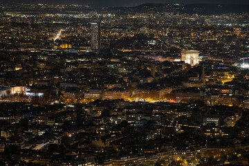 Aerial view of the glowing cityscape with the illuminated Arc de Triomphe and the Montparnasse Tower piercing the dark sky, Paris, Ile-de-France, France.