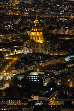 Aerial view of golden dome of Les Invalides piercing the dark, a beacon amidst the illuminated cityscape below, its warm light contrasting with the cool night air, Paris, Ile-de-France, France.