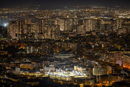 Aerial view of the illuminated cityscape reveals a tapestry of twinkling lights and shadows, the vibrant glow contrasting with the inky sky, Paris, Ile-de-France, France.