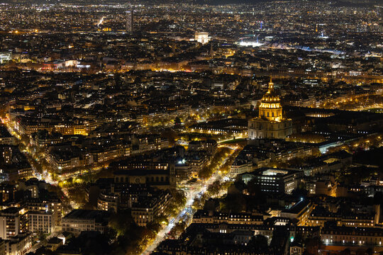Aerial view of the golden dome of Les Invalides glows amidst the dark tapestry of Paris, punctuated by the distant sparkle of the Eiffel Tower, Paris, Ile-de-France, France.