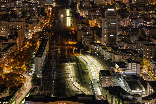 Aerial view of the illuminated railway lines cutting through the heart of the city, a stark contrast against the dark urban fabric, Paris, Ile-de-France, France.