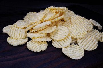 Round corn chips in a pile. Corrugated corn chips on a dark background.