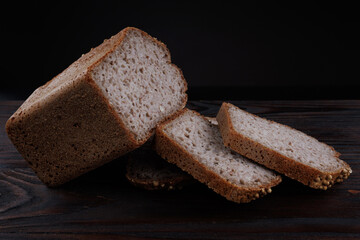 Half a loaf and pieces of sliced buckwheat bread on a dark wooden background.