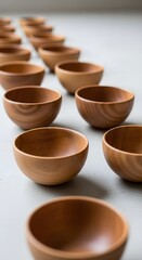 A row of empty wooden bowls arranged in a diagonal line on a light surface, showcasing their smooth finish and natural wood grain patterns