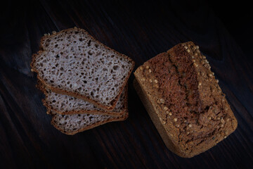 Half a loaf and pieces of sliced buckwheat bread on a dark wooden background.
