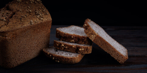 Half a loaf and pieces of sliced buckwheat bread on a dark wooden background.
