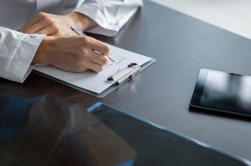 Fototapeta premium Male doctor writing notes on tablet at desk close-up