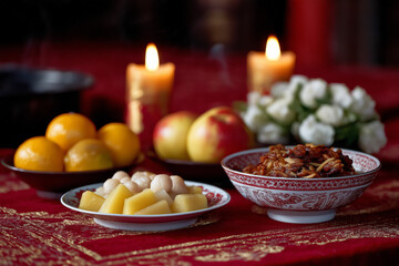 Traditional asian ancestral offering with candles and fruits on red tablecloth