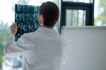 Physician in lab coat analyzing transparent MRI film
