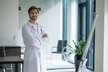 Fototapeta premium Young male doctor standing next to flipchart in clinic
