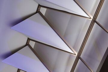 Close up view of a modern ceiling with architectural triangular panels and linear metal framing, illuminated by ambient purple light