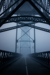 A fog-shrouded view inside the Dom Lu&iacute;s I Bridge in Porto, Portugal, with the steel arches fading into mist above an empty roadway. The atmosphere is eerie, quiet, and beautifully geometric.