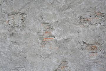 A detailed view of a rough, weathered plaster wall texture, revealing glimpses of the underlying aged brickwork. A raw, urban background.