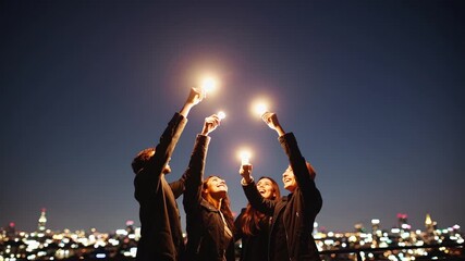 Friends celebrate together at night in a cityscape with lights and sparklers