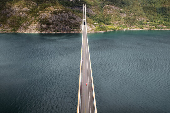 Aerial view of the Hardanger Bridge stretching across the serene Hardangerfjord, connecting mountainous landscapes under a vast sky, Vallavik, Vestland, Norway.