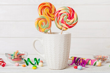 Colorful candies in cup on table on light background background. Large swirled lollipops. Creative concept of a jar full of delicious sweets from the candy store
