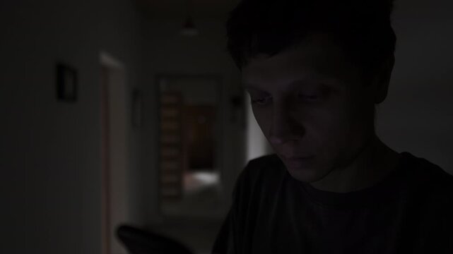 Man secretly texting on his phone in a dark hallway, hiding private messages and avoiding being seen