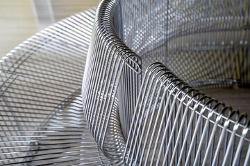 Close-up on the spiraling curves of a futuristic chrome wire mesh chair or bench, emphasizing the...