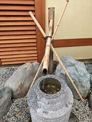 Traditional Japanese bamboo water fountain in a Zen garden. Stone basin, flowing water, and natural materials create a peaceful, meditative atmosphere typical of Japanese aesthetics.
