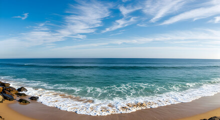 Obraz premium Panoramic View of Tranquil Ocean Waves Crashing on Golden Sands Under a Bright Blue Sky with Soft Clouds and the Distant Horizon in a Peaceful Beach Setting