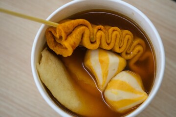 Top view of Korean street food dish with fish cakes and skewered eomuk served in hot savory broth inside a paper cup.
