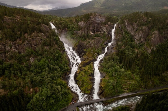 Aerial view of the majestic twin waterfalls cascading down rugged cliffs amidst verdant forests, a symphony of white water and green foliage, Latefossen, Skare, Vestland, Norway.