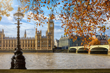 Autumn day view of the Big Ben clock tower and Westminster Bridge in London, England, with golden leaves on the trees