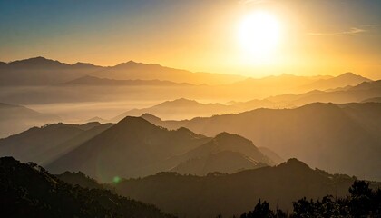 A breathtaking sunrise casts a warm golden glow over multiple layers of silhouetted mountain ranges, with mist filling the valleys below.