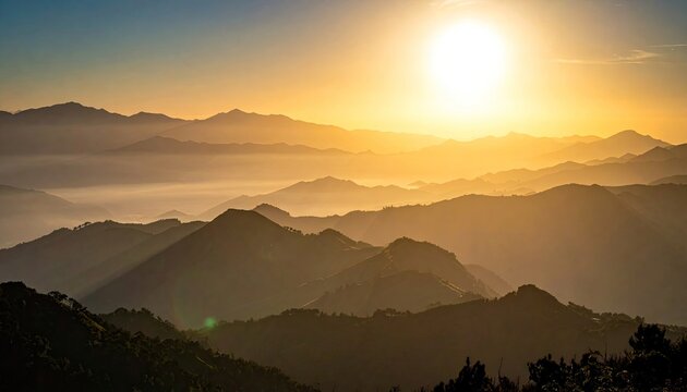 A breathtaking sunrise casts a warm golden glow over multiple layers of silhouetted mountain ranges, with mist filling the valleys below.