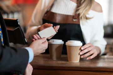 The barista accepts a credit card as a businessman pays for takeaway coffee showing a smooth modern cashless cafe interaction